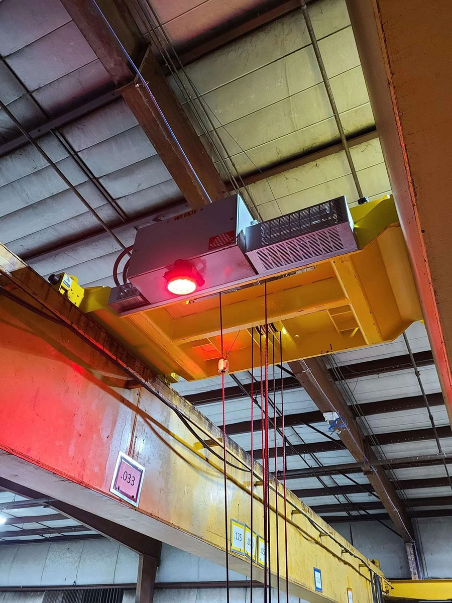 Laser industriel rouge mont&eacute; sur un pont roulant jaune projetant un signal de s&eacute;curit&eacute; au sol en entrep&ocirc;t.