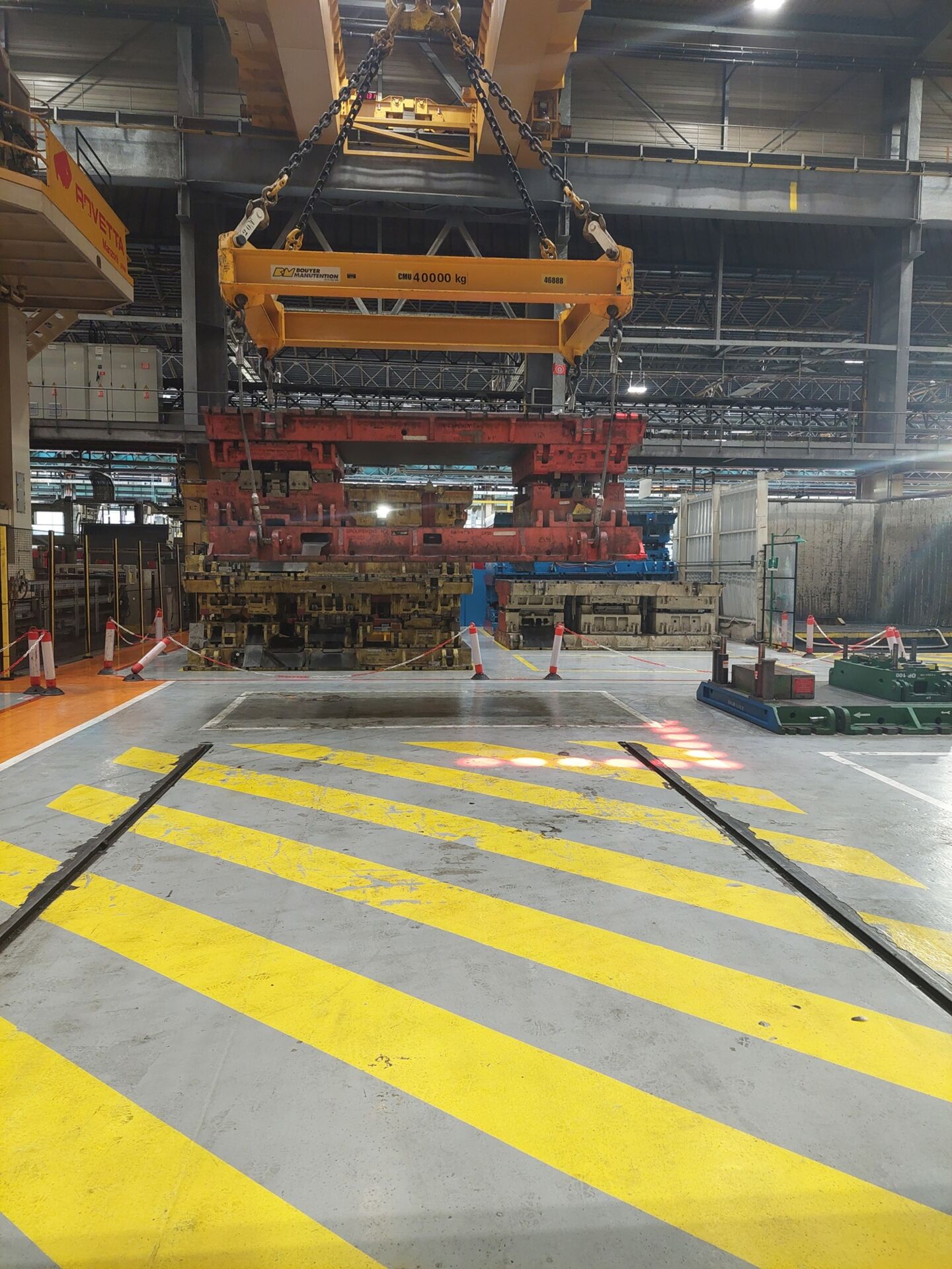 Zone de danger d&eacute;limit&eacute;e par des points lumineux rouges au sol sous un pont roulant soulevant une charge industrielle lourde.
